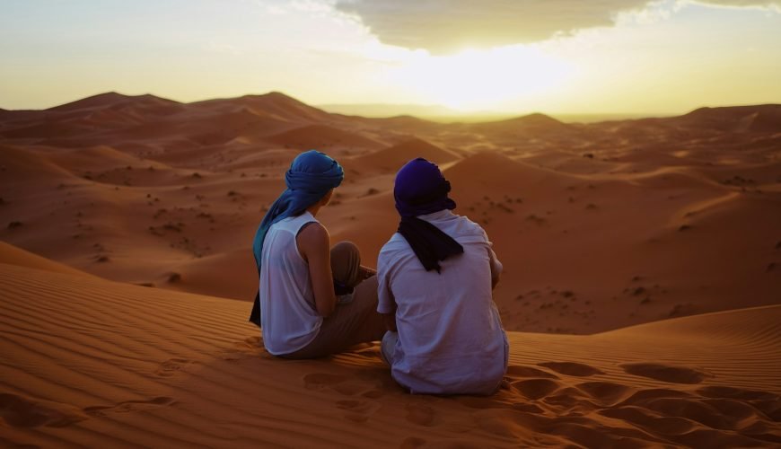 two men sitting on sand dunes