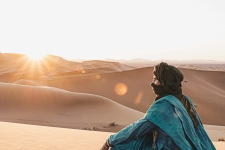 woman in blue hoodie sitting on sand during sunset