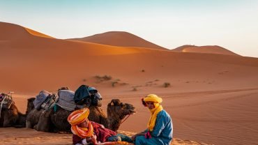 man in yellow robe sitting on brown sand during daytime