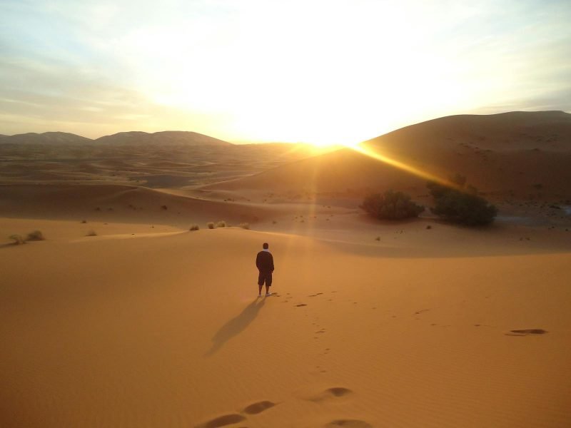 Silhouette d'un homme marchant le long des dunes de sable au lever du soleil dans le désert du Sahara.