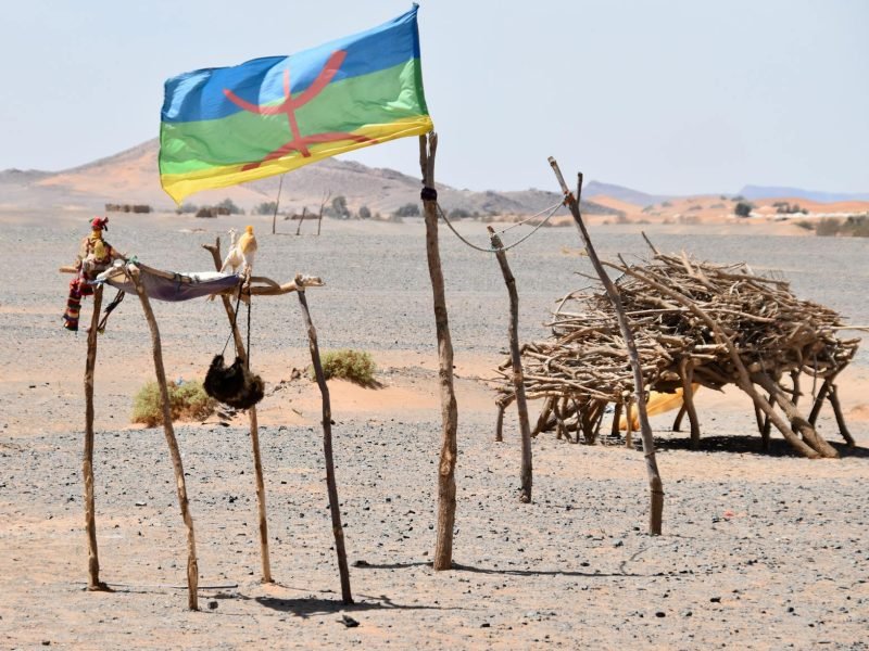 Colorida bandera bereber ondeando en el desierto de Merzouga, Morocco, acentuada por estructuras rústicas de madera.